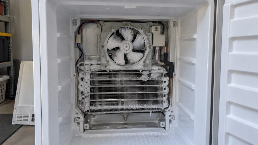 The rear evaporator panel of an LG upright freezer removed, showing the evaporator fan with frost on its blades