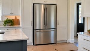 A stainless steel LG French door refrigerator freshly placed in a kitchen alcove between cabinets, with protective cardboard still on the floor