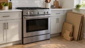 A freestanding stainless steel range in place between kitchen cabinets with flattened cardboard packaging beside it